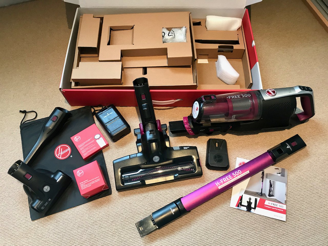 A flat lay showing the contents of the H Free 500 model. At the rear the empty box containing the cardboard packing. In front of the box (l to r) the accessory bag, crevice tool, pet brush, filter & 2 battery packs & the unassembled cordless vacuum
