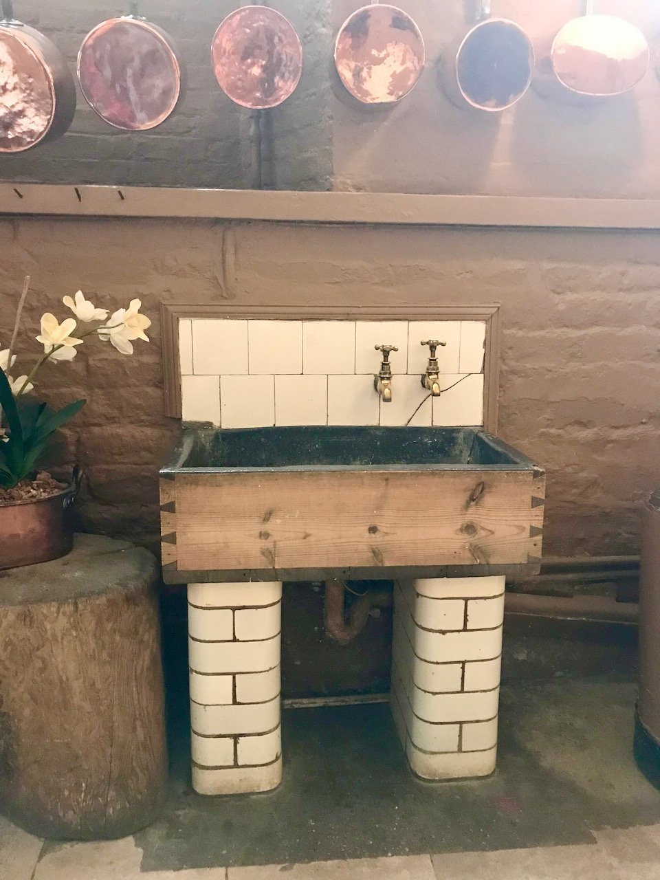 a wooden lead lined sink on tiled pillars with two taps out of the tiled splashback