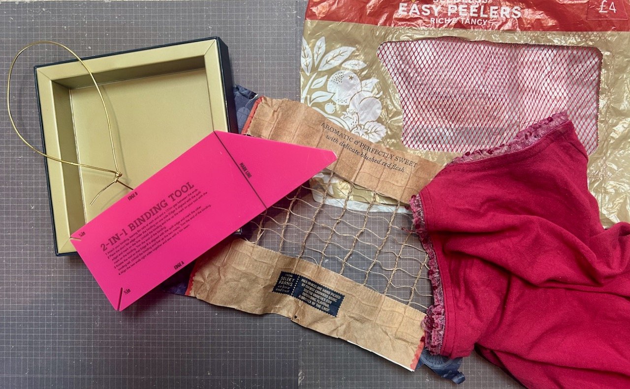 A gold cardboard box and tie, a binding tool, mesh and an old camisole top