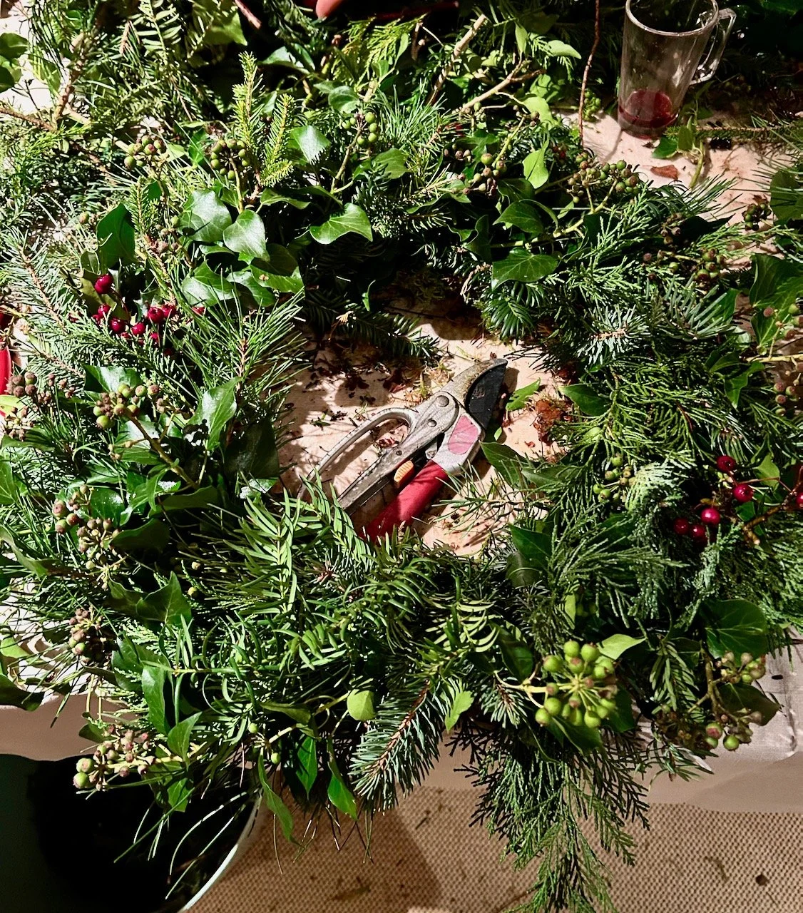 My wreath after adding greenery, some ivy flowers and a few red berries - secateurs at rest in the middle of the wreath