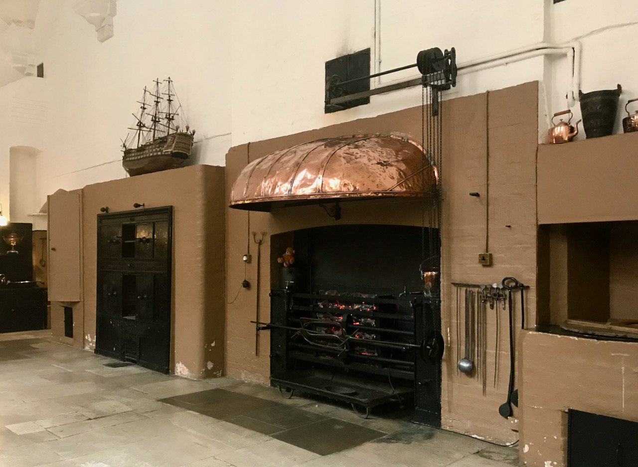 the ovens along one side of the kitchen with an open fire with a large copper 'hood'