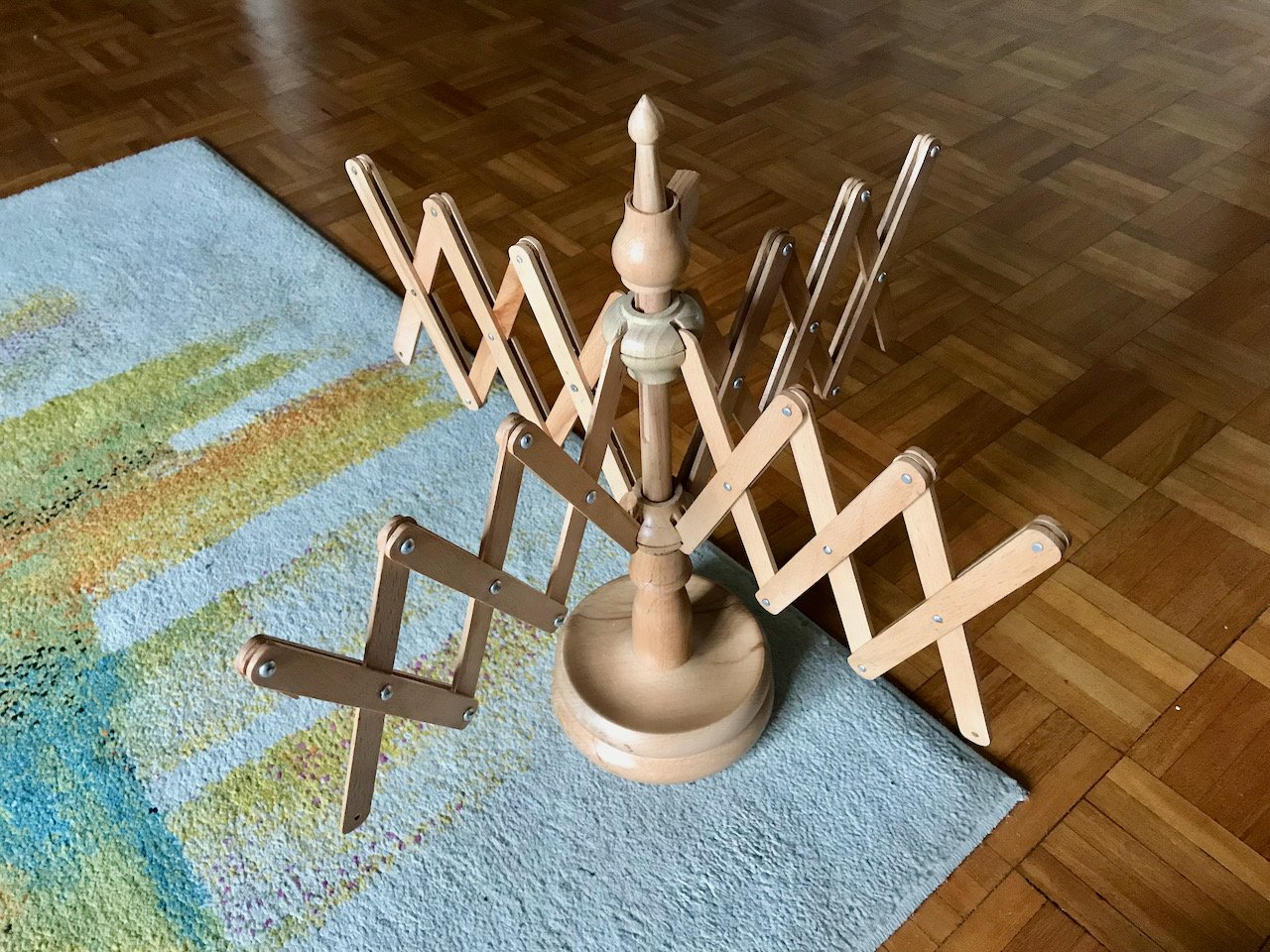 a wooden yarn swift photographed on the floor, part on a rug