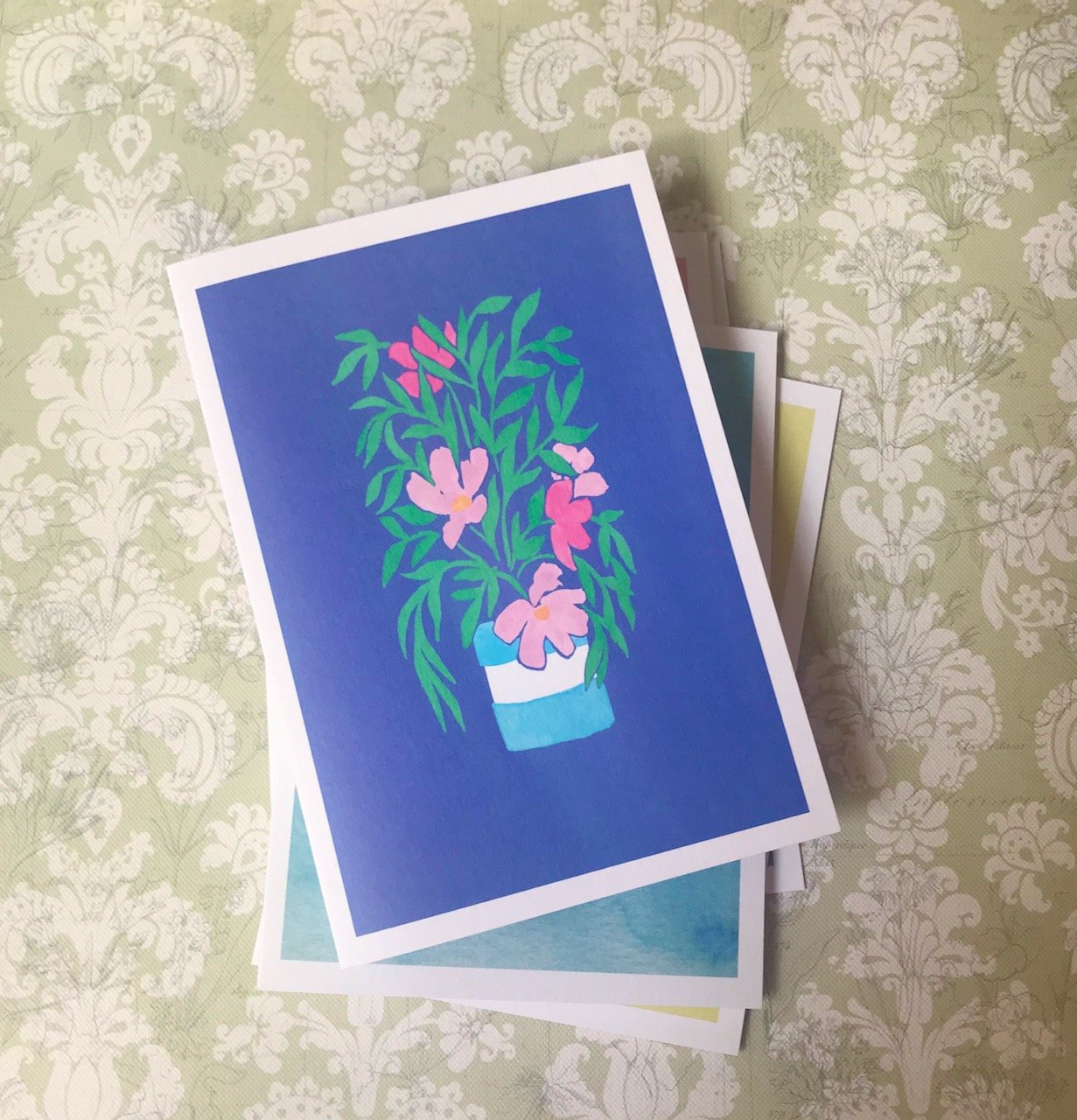 A pink flowering plant with tall green leaves in a blue and white pot on a purpley/blue background