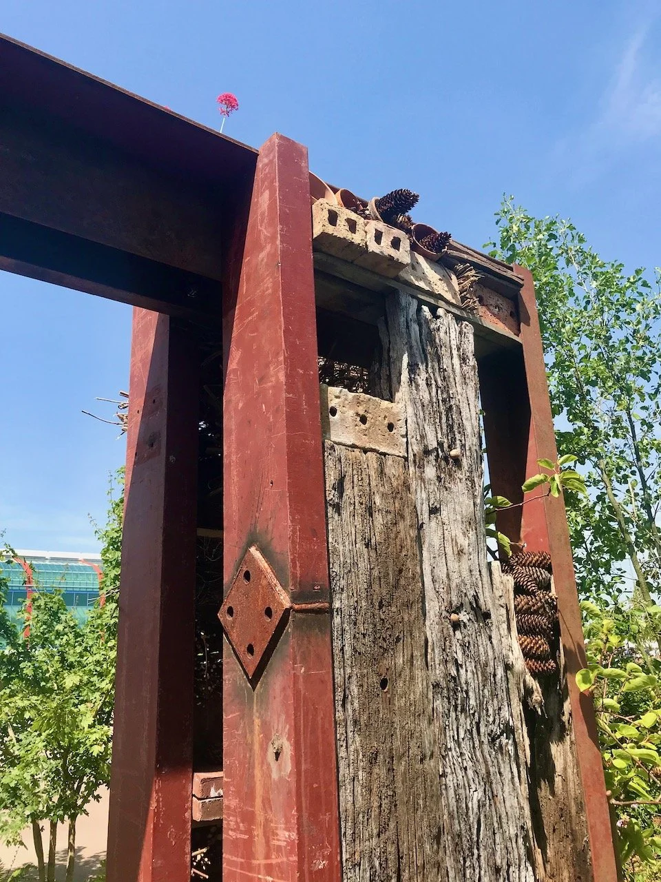 The top of the steel beamed bug hotel structure showing sleepers, bricks and pine cones in terracotta pots