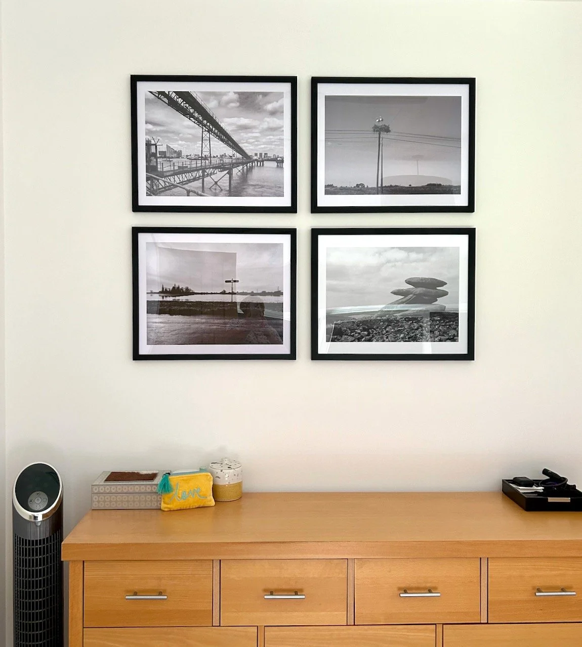 The four black and white pictures hung on the wall above a light wood chest of drawers