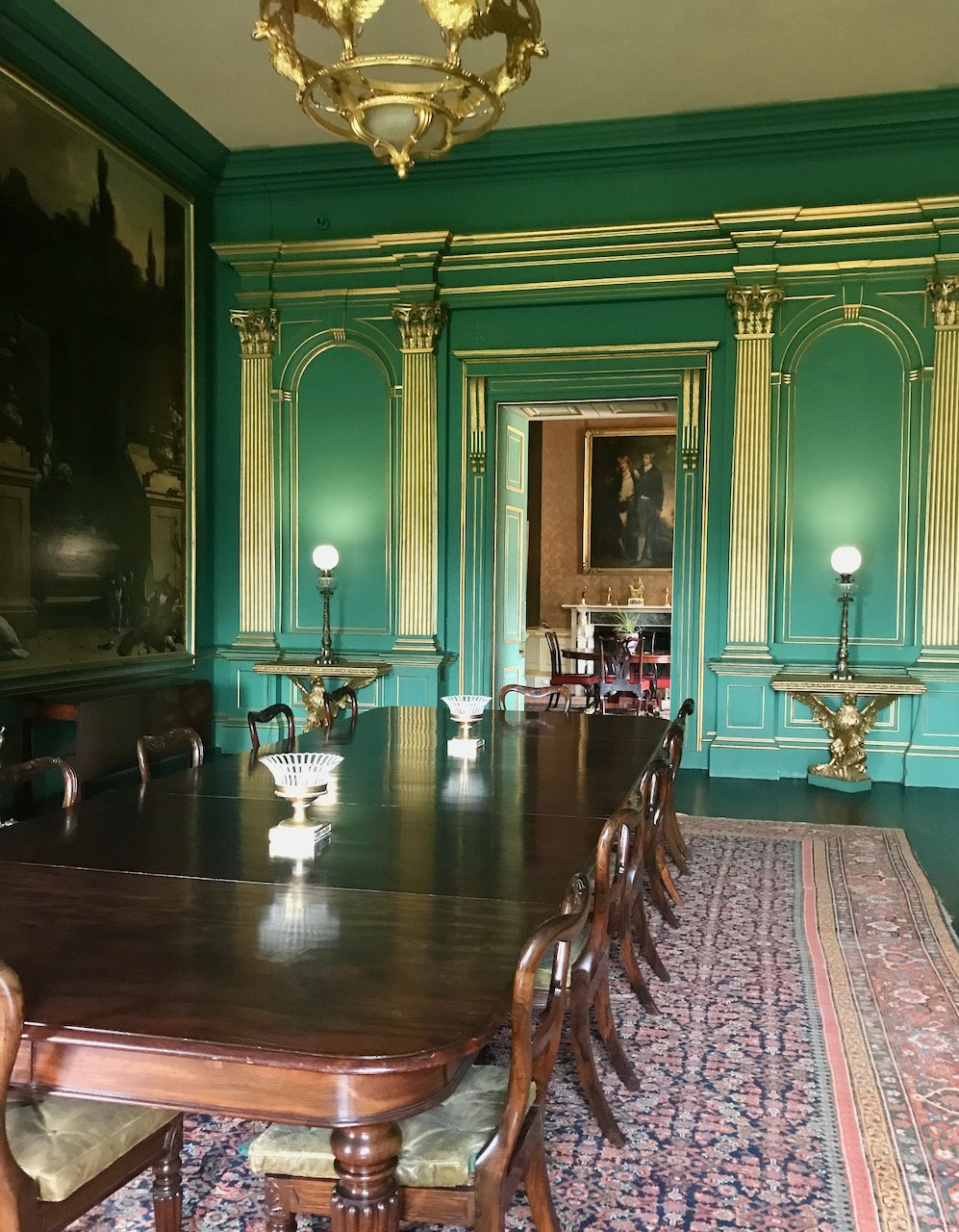in the green & gold dining room looking at the otherside of the table, with a rug and route through to the next room