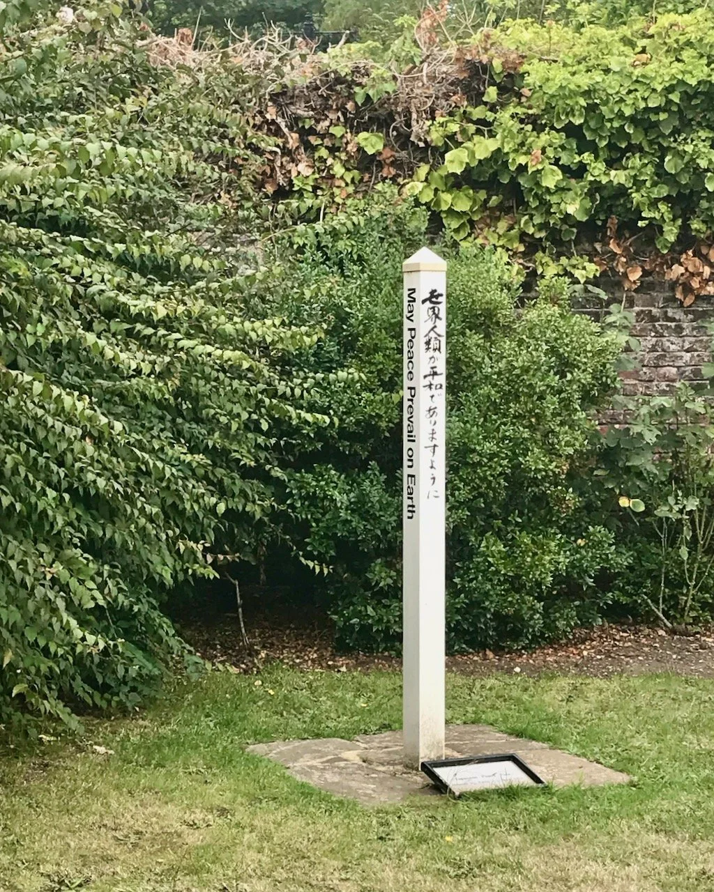 A wooden post painted white with black lettering - May Peace Prevail on Earth - also in unknown script