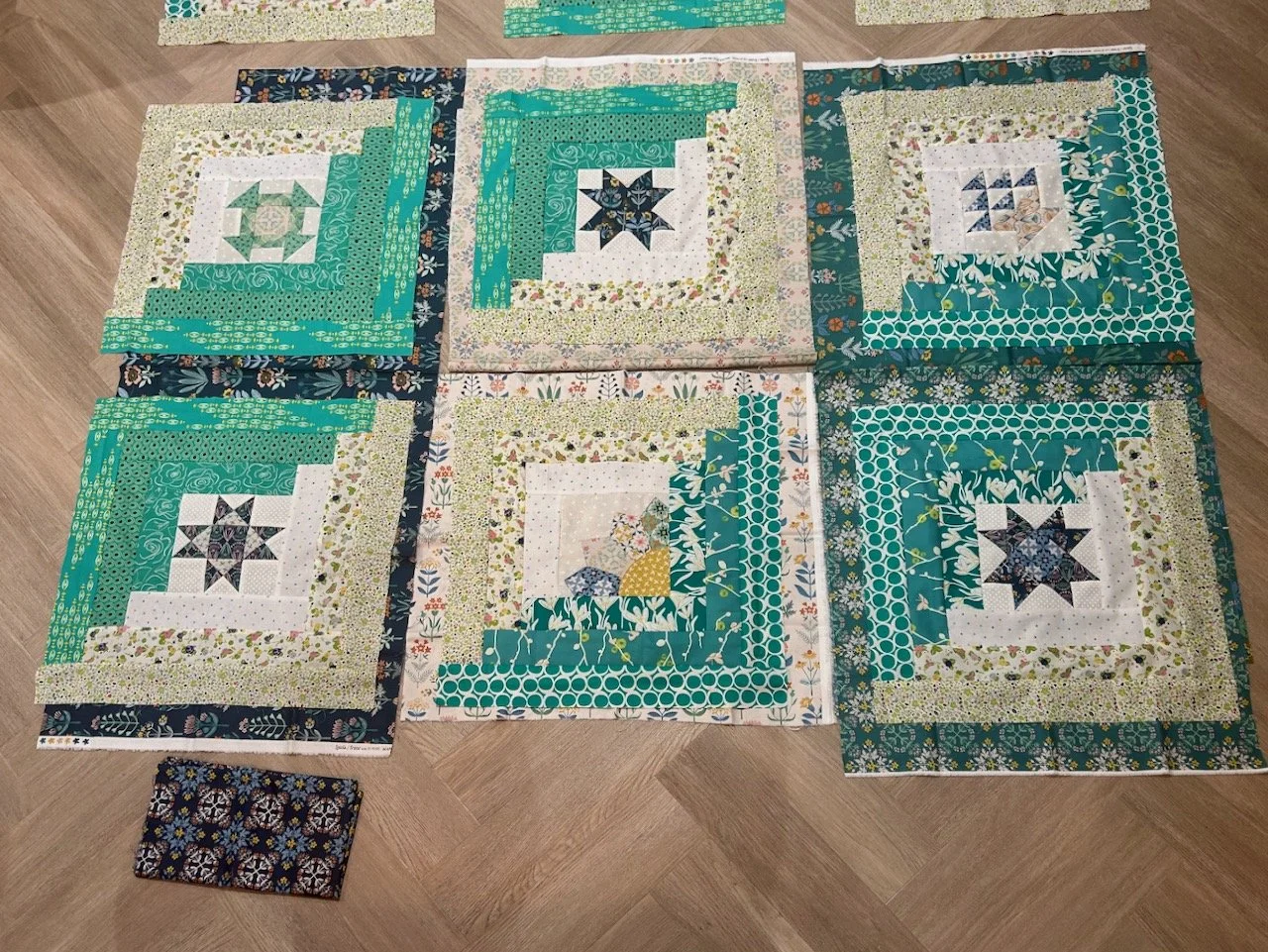 six of the monthly blocks laid on top of various greens, creams and navy fabrics to test out border options