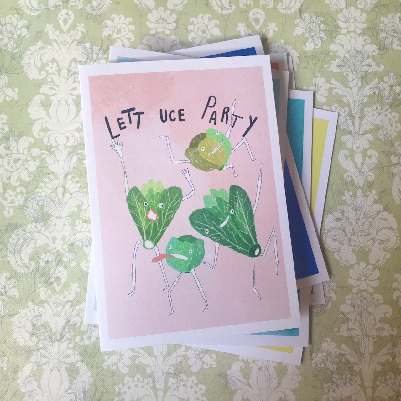 Four lettuces with arms and legs (obviously) dancing with the words Lettuce Party above on a pale pink background