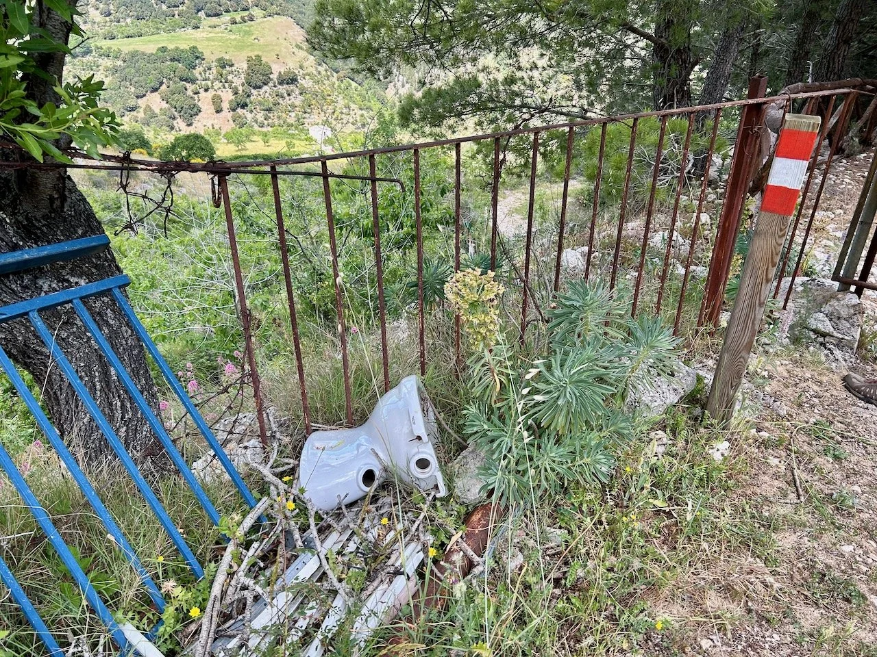 Alongside the red/white stripe topped pole is a discarded WC with a homemade metal gate tied to the tree