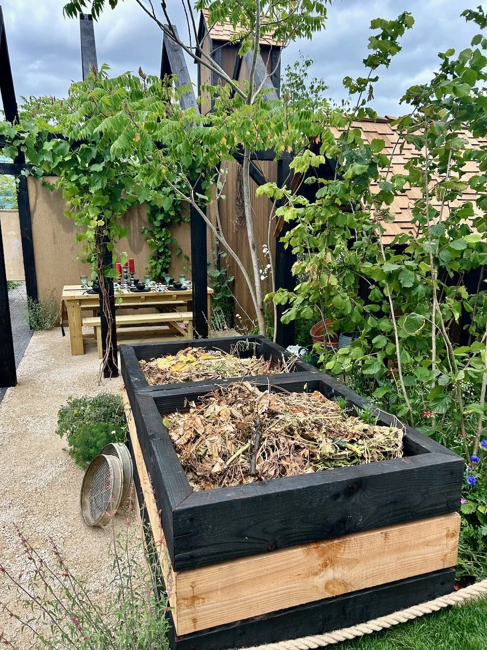 Two open compost bins made from squares of wood, with the dining area behind