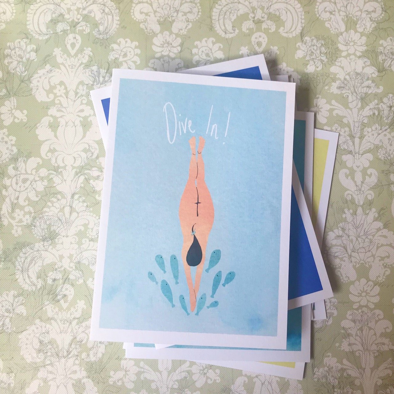 A pale blue background, below the words Dive in! is a female naked body diving into the water, the splashes are small blue fish