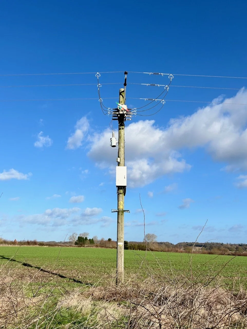 Looking up at the blue skies and power lines above and spotting a large on/off switch at the top of the telegraph pole