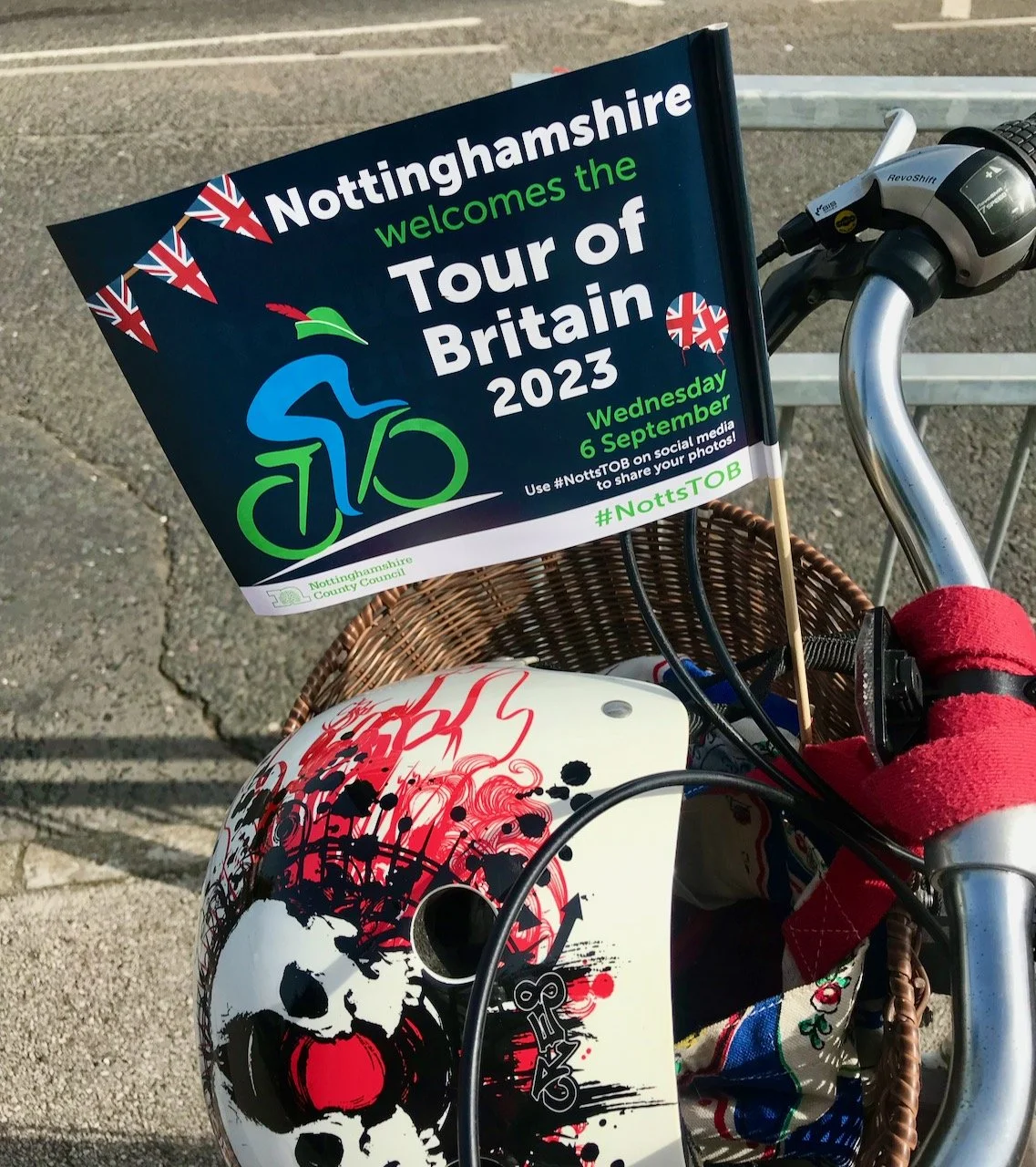 A paper Tour of Britain flag in my bike's wicker basket along with my cycling helmet as we stand on the roadside waiting for the race to go past
