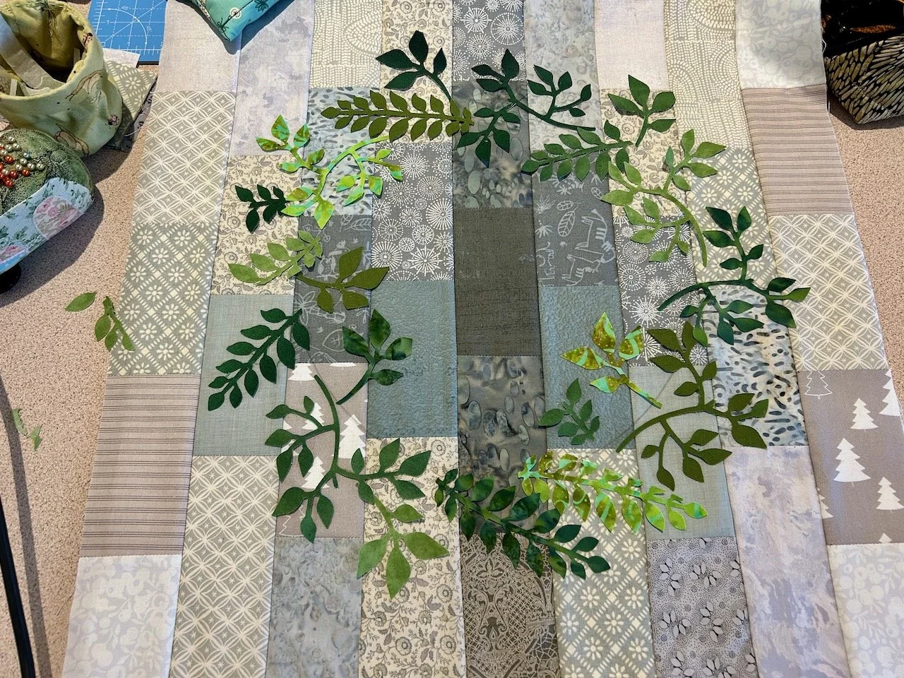 a circle of varying green leaf shapes on a grey patchwork panel