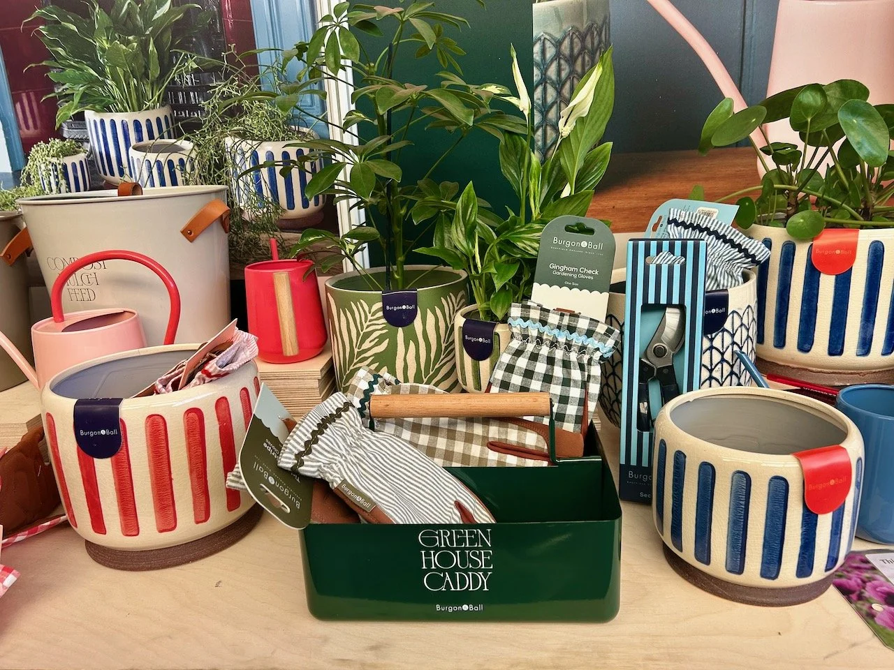 A colourful display of planters, pots, watering cans, gardening gloves & a green house caddy