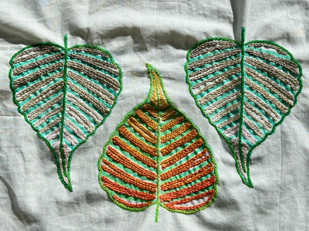 All three motifs outlined and filled with chain stitches in neutral colours for the two outside leaves and warm oranges and yellows for the middle motif