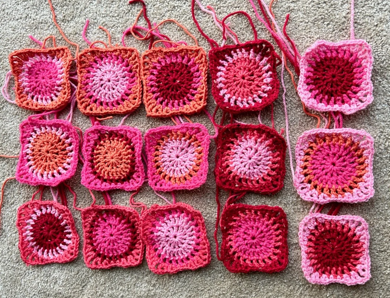 Fifteen mid-sized granny squares in shades of pinks, red and orange - each has a different colour combination with two circles which are then squared off