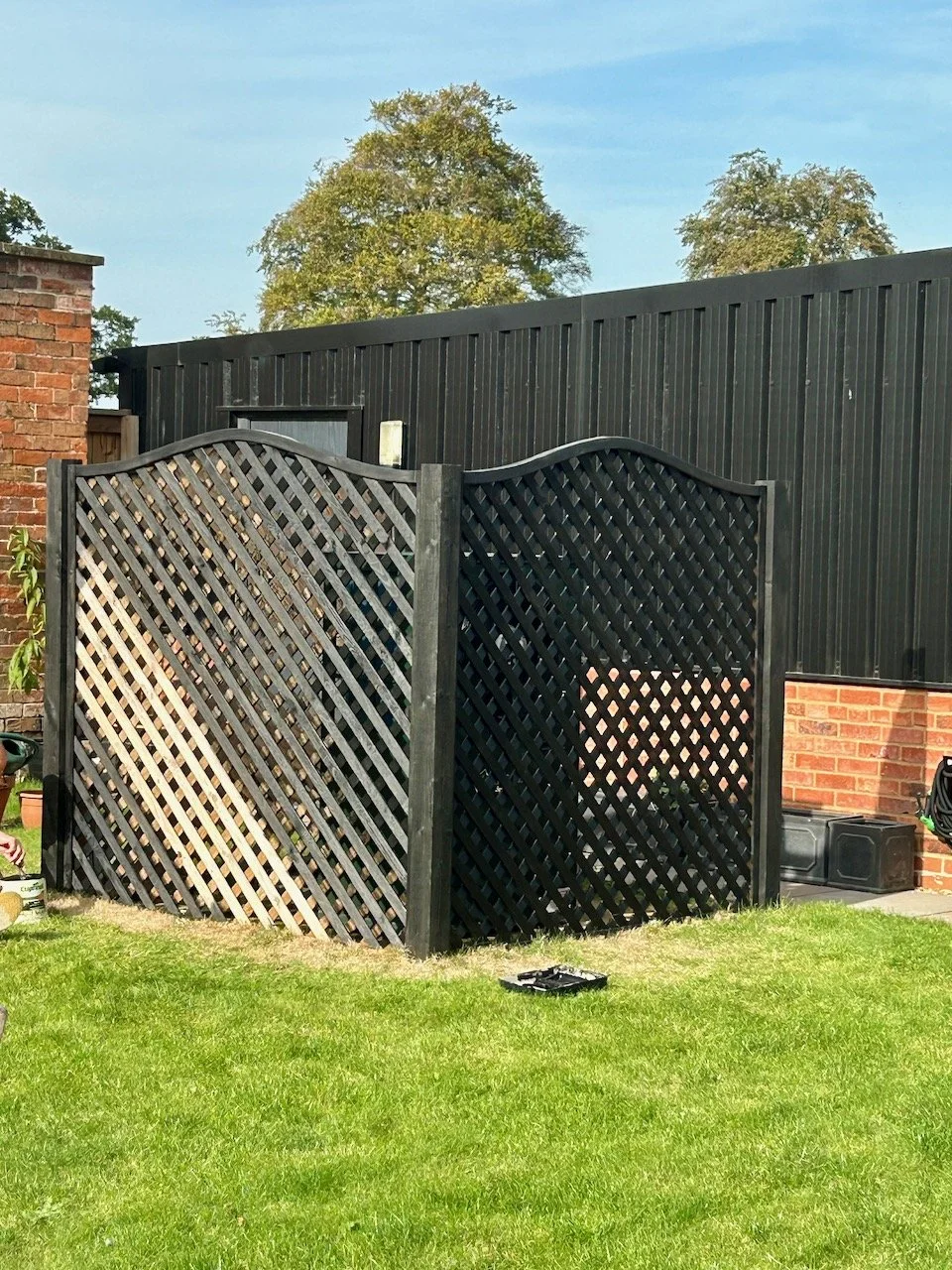 Part-way through painting the wooden trellis around our heat pump black to blend in with the garage behind