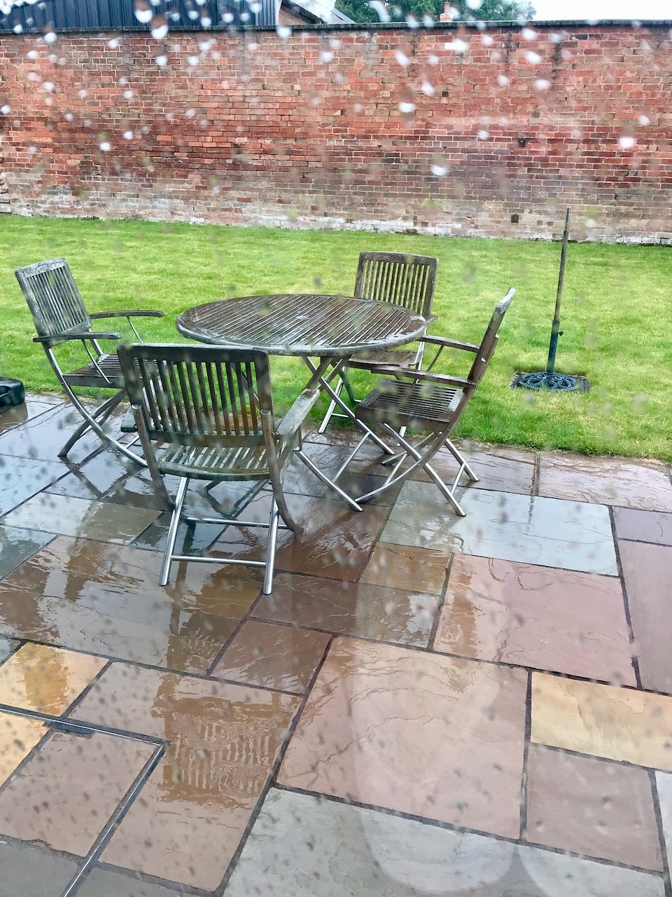 A very wet patio and patio furniture with rain on the window