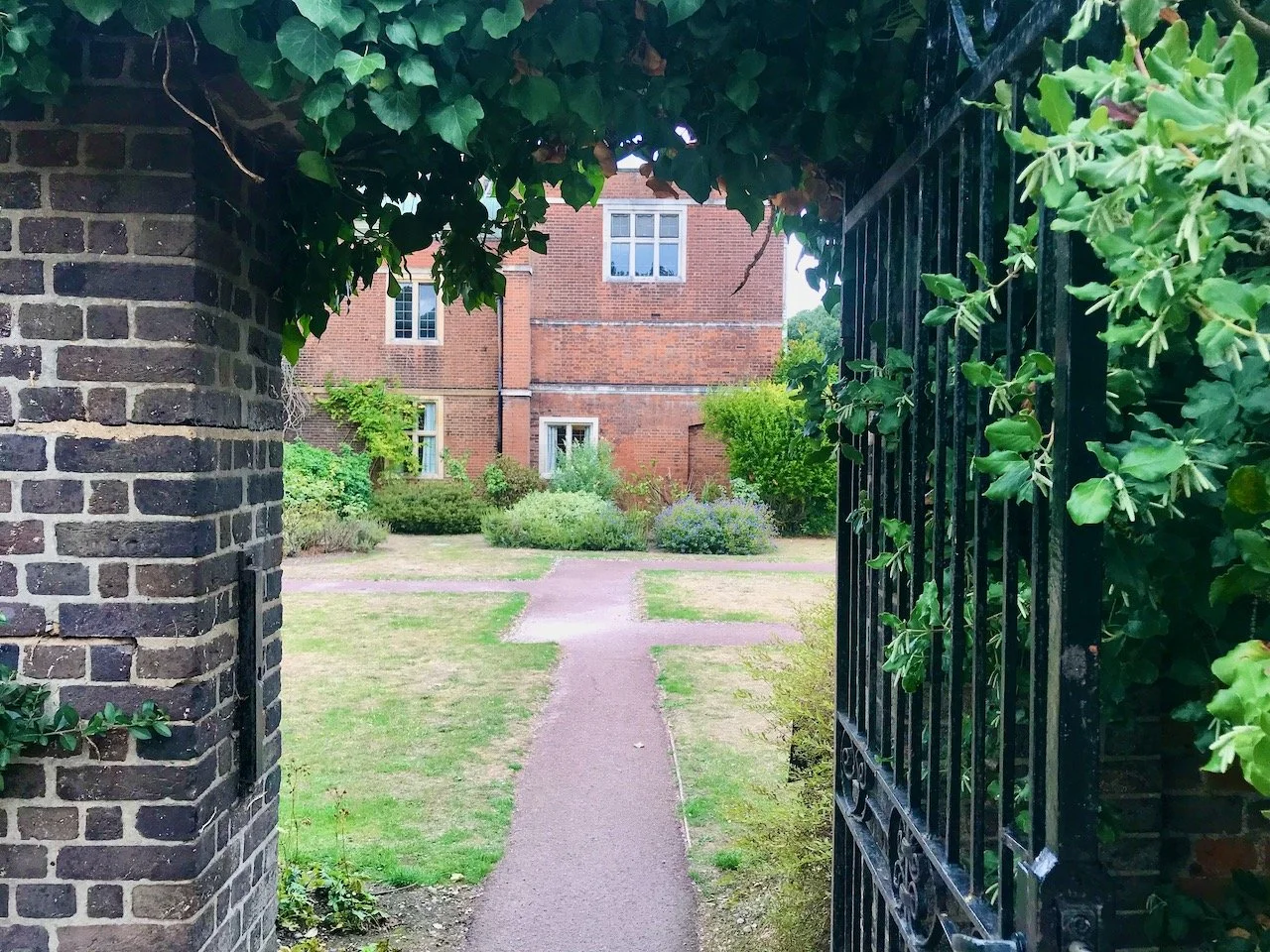 Looking back through the gate towards Charlton House with ivy over the bricked arch and the wrought iron gate open on the right hand side