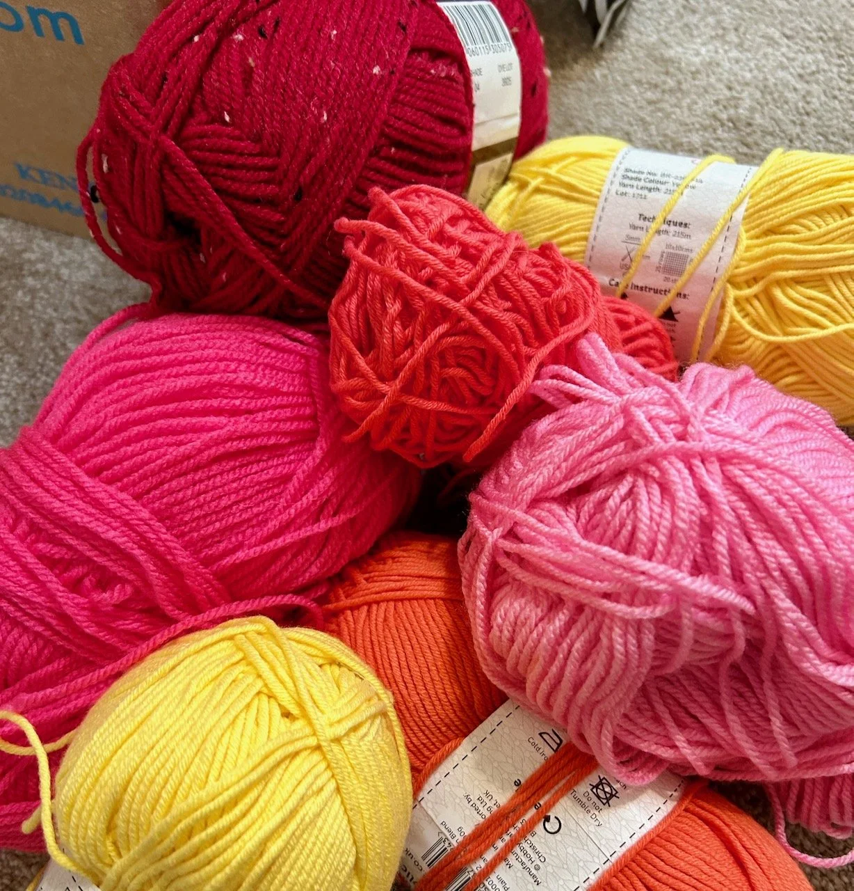 Balls of wool on the floor - reds, pinks, orange, coral & yellow