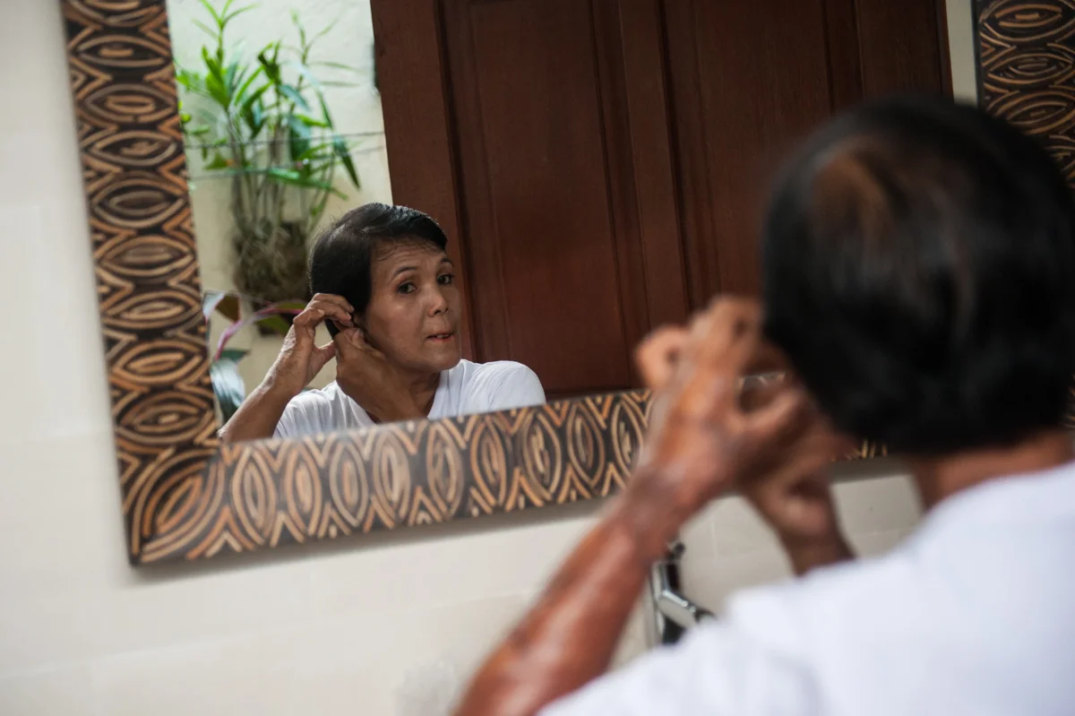 Yayuk puts on an earring in her workplace in Kerobokan, Bali. Besides watering the plants, her tasks include doing the laundry, cleaning the house and feeding the two dogs.