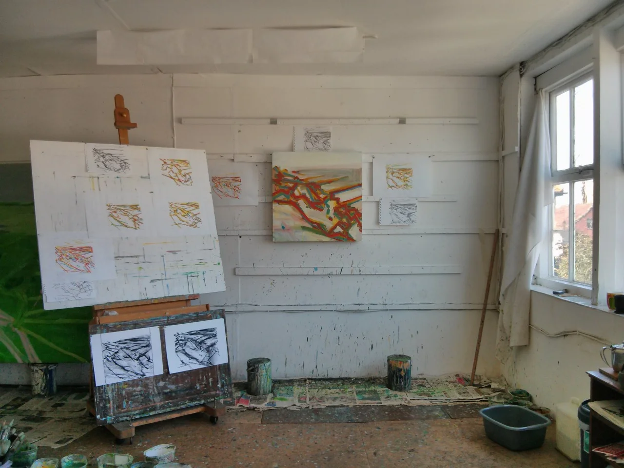 The studio this afternoon. Several oil pastel drawings and charcoal drawings on the wall and the board. After this photograph was taken I added alot of grey to the painting, didn’t like it so scraped it all off, repainted the canvas white and painted the network of lines in first yellow, then blue and then red. It now looks more bleached then this.