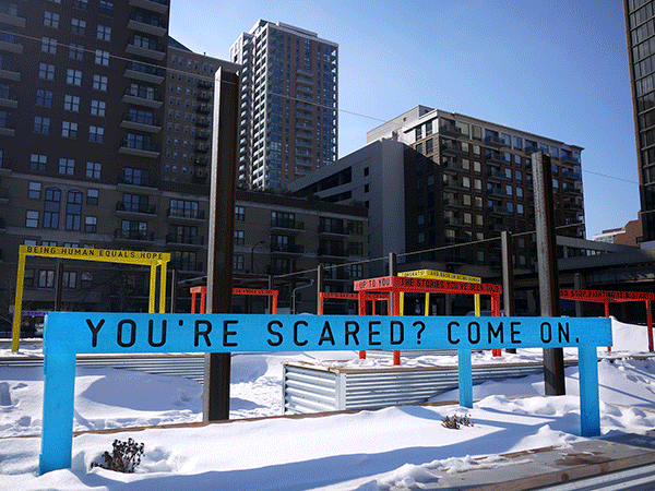 “Being Human Equals Hope” outdoor installation by Matthew Hoffman, yellow frame structure in snowy Chicago park with high-rise buildings.