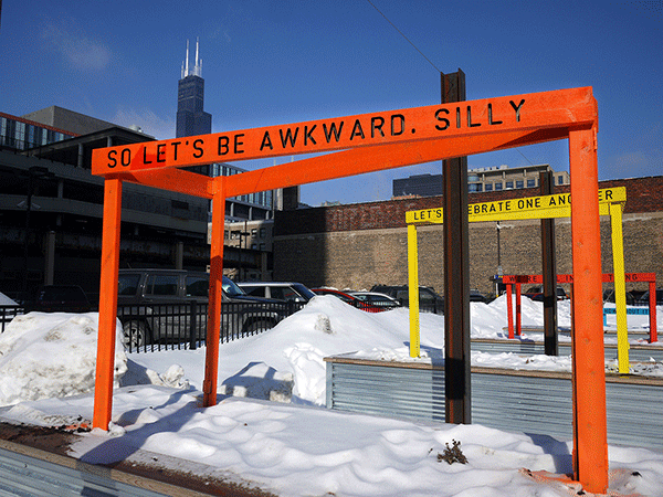“Being Human Equals Hope” outdoor installation by Matthew Hoffman, yellow frame structure in snowy Chicago park with high-rise buildings.
