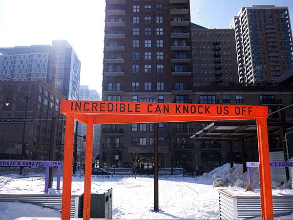 “Being Human Equals Hope” outdoor installation by Matthew Hoffman, yellow frame structure in snowy Chicago park with high-rise buildings.