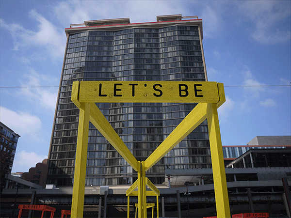 “Being Human Equals Hope” outdoor installation by Matthew Hoffman, yellow frame structure in snowy Chicago park with high-rise buildings.