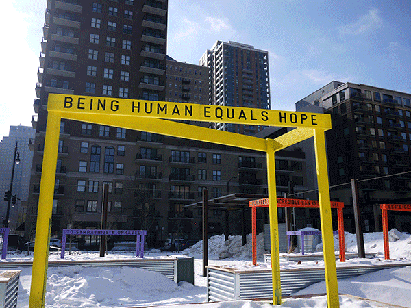 “Being Human Equals Hope” outdoor installation by Matthew Hoffman, yellow frame structure in snowy Chicago park with high-rise buildings.
