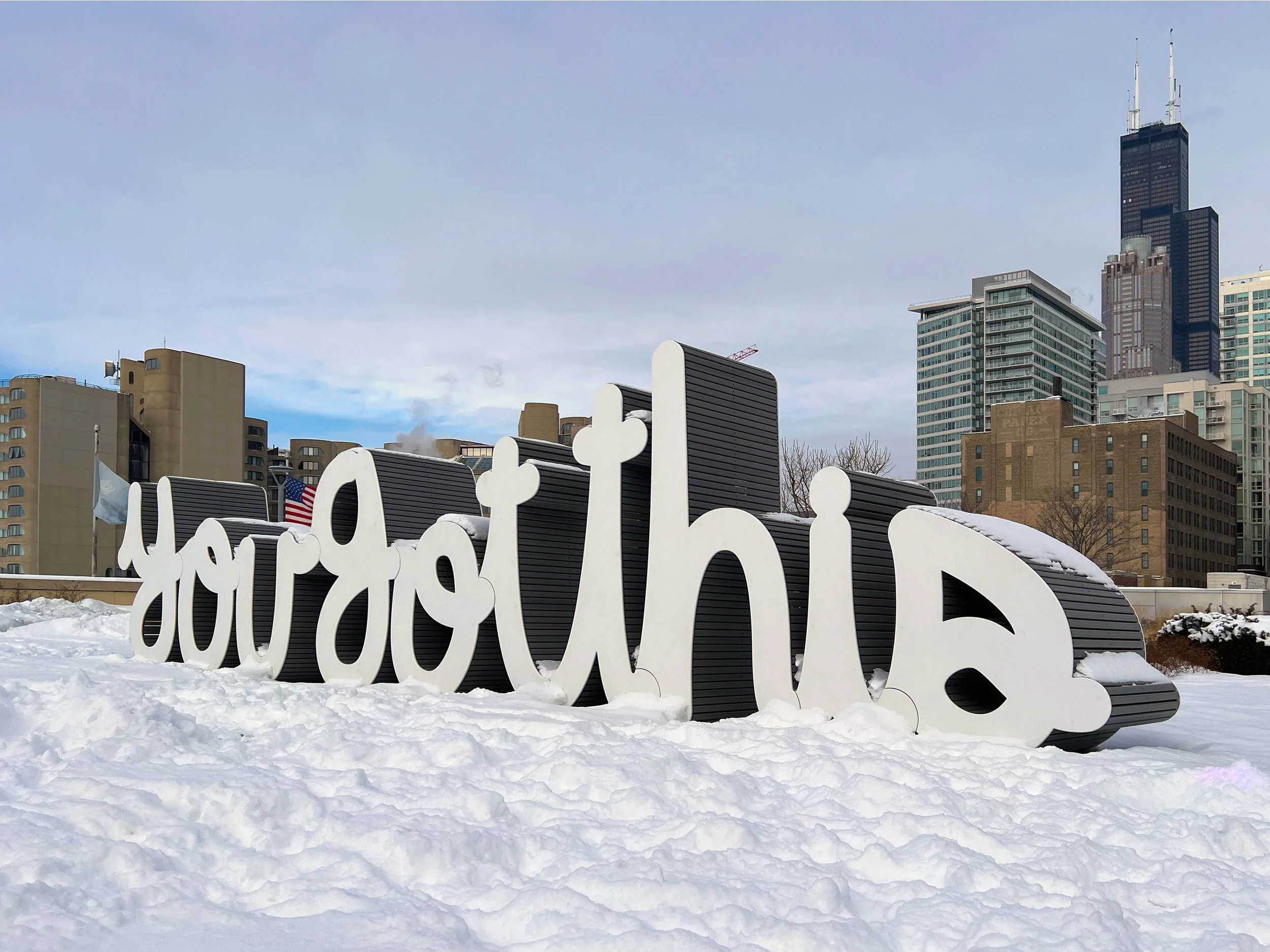 Matthew Hoffman’s “You Got This” public sculpture in Chicago covered in snow with the city skyline rising behind the large-scale interactive artwork.
