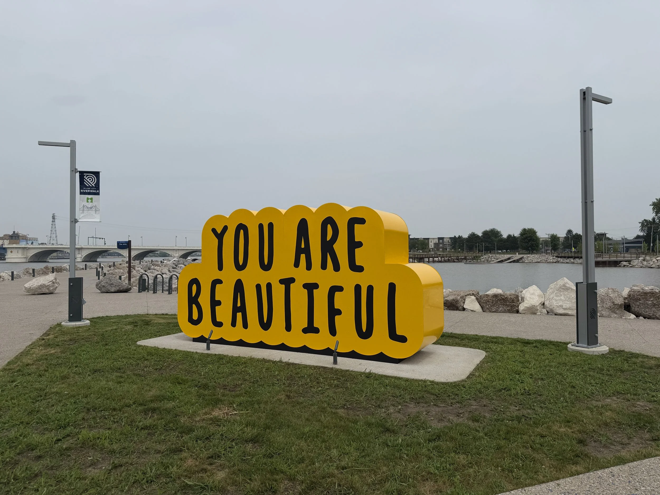Double-sided public sculpture by Matthew Hoffman reading "You Are Doing Great" and "You Are Beautiful" along Toledo's Glass City Riverwalk.