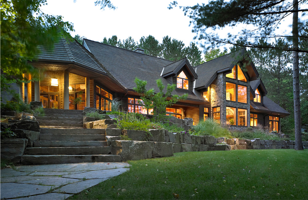   The rear of the boldly defined home sites majestically on a stone pedestal. Walls of glass connect every interior space to the natural environment from this elevated perch.     