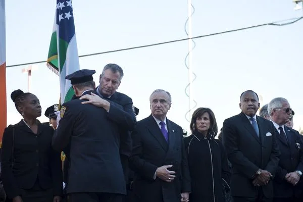 The official Twitter account of City Hall published a photograph showing Mayor Bill de Blasio warmly hugging an unidentified uniformed police officer on Saturday. This photograph was published in answer to several damaging images showing NYPD police officers turning their backs to the embattled mayor and to a brutal photograph of an airplane pulling a banner denouncing the mayor on Friday. Under pressure by police unions and police reform activists, it's not known if the police officer receiving the hug is employed by the NYPD, or if a general appreciation by the mayor of just any uniformed police officer was the sensibility that City Hall wanted to invoke in an effort to appease disgruntled police unions. Source : NYC Mayor's Office/Official Twitter Account