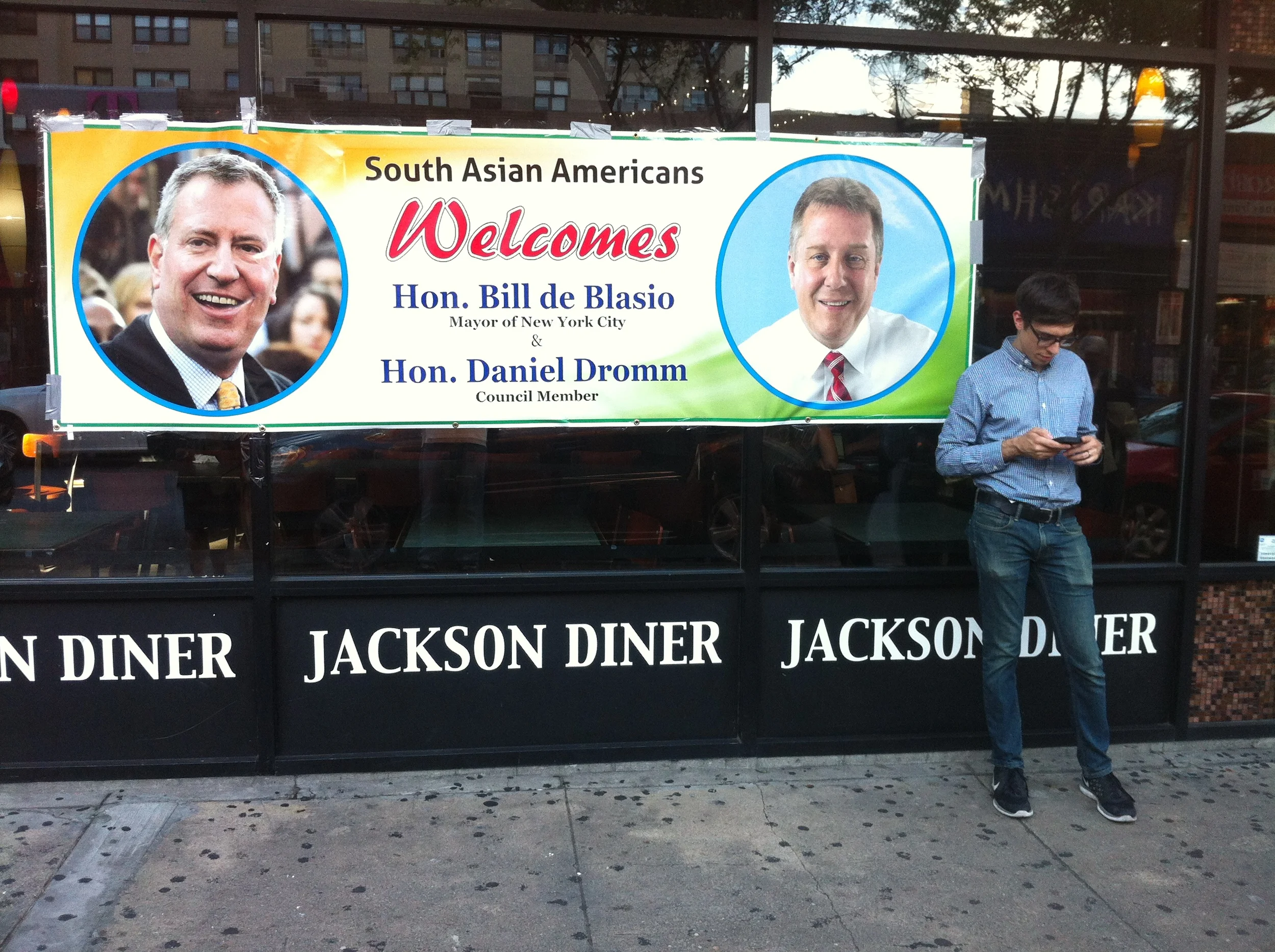 The giant welcoming banner outside the Jackson Diner , location of a small money donation fundraiser to benefit the committee to reëlect Mayor Bill de Blasio (D-New York City). The fundraiser was hosted by New York City Councilmember Daniel Dromm (D-Jackson Heights). Source : Louis Flores/Progress Queens