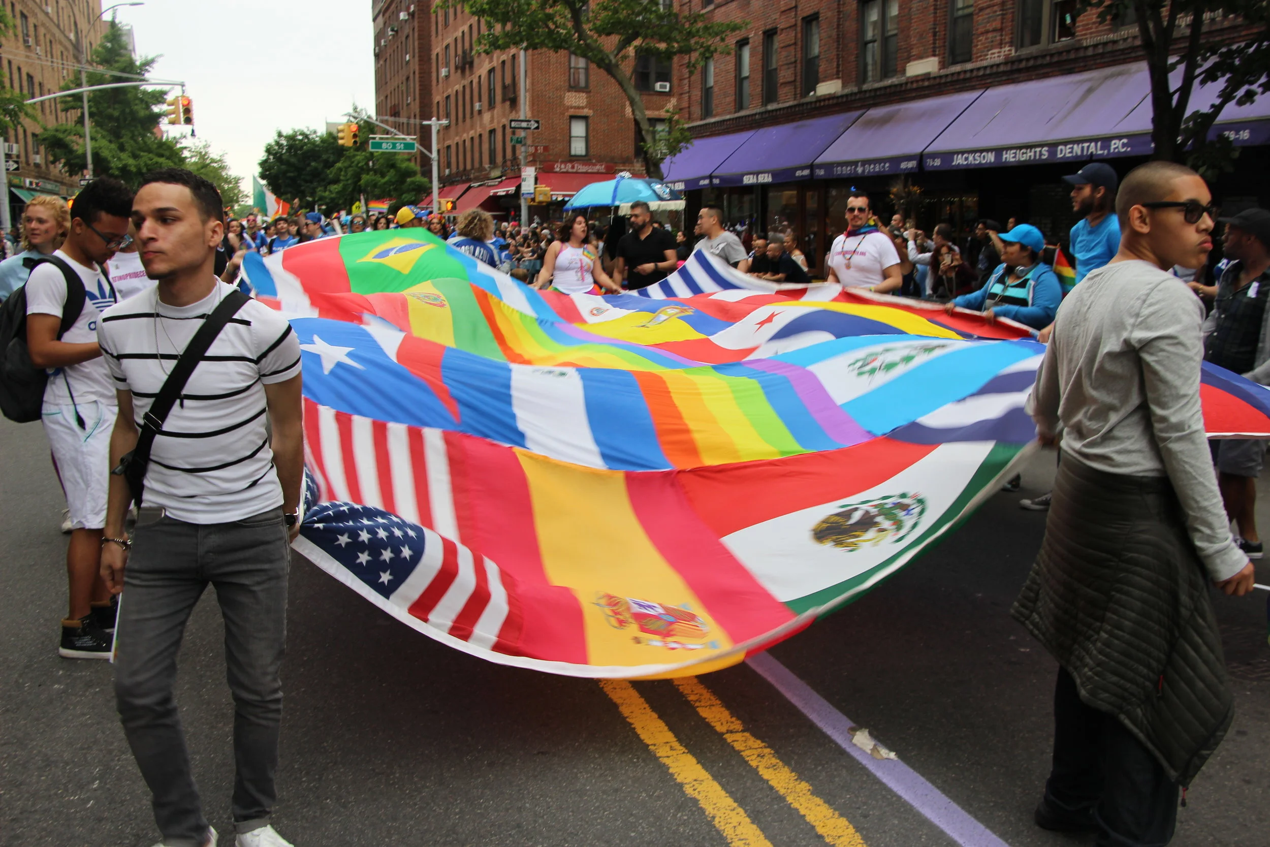 To signify LGBT diversity, some participants in the Queens Pride Parade carried a giant patchwork of various flags, including the Rainbow Flag , the latter which was designed by the late Gilbert Baker . The flags represented some of the backgrounds of the LGBT community in Queens. Source : Pauline Park/Used With Permission