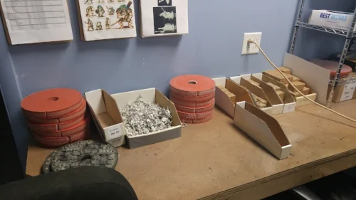 A big bin of hero figures. The orange disc are silicon molds used to make those figures, and the brown boxes to the side are older figures which have since been discontinued. Above the box, you can see some of the design concepts on a clipboard.