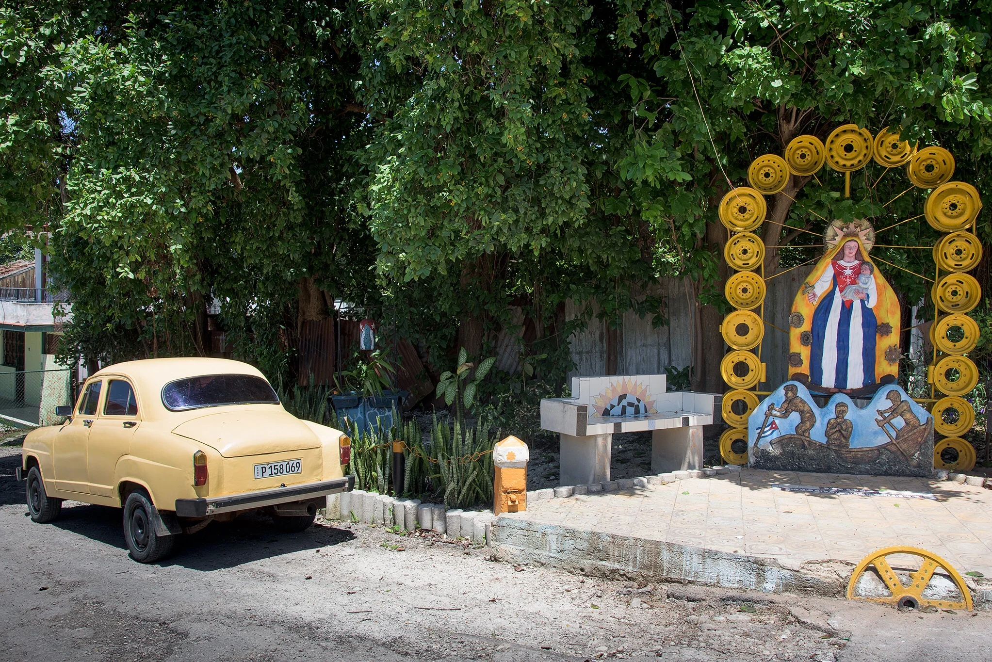 Another old Soviet era car sits near "Our Lady of Guadelope" art work created from old tire rims at the Muraleando Project. 