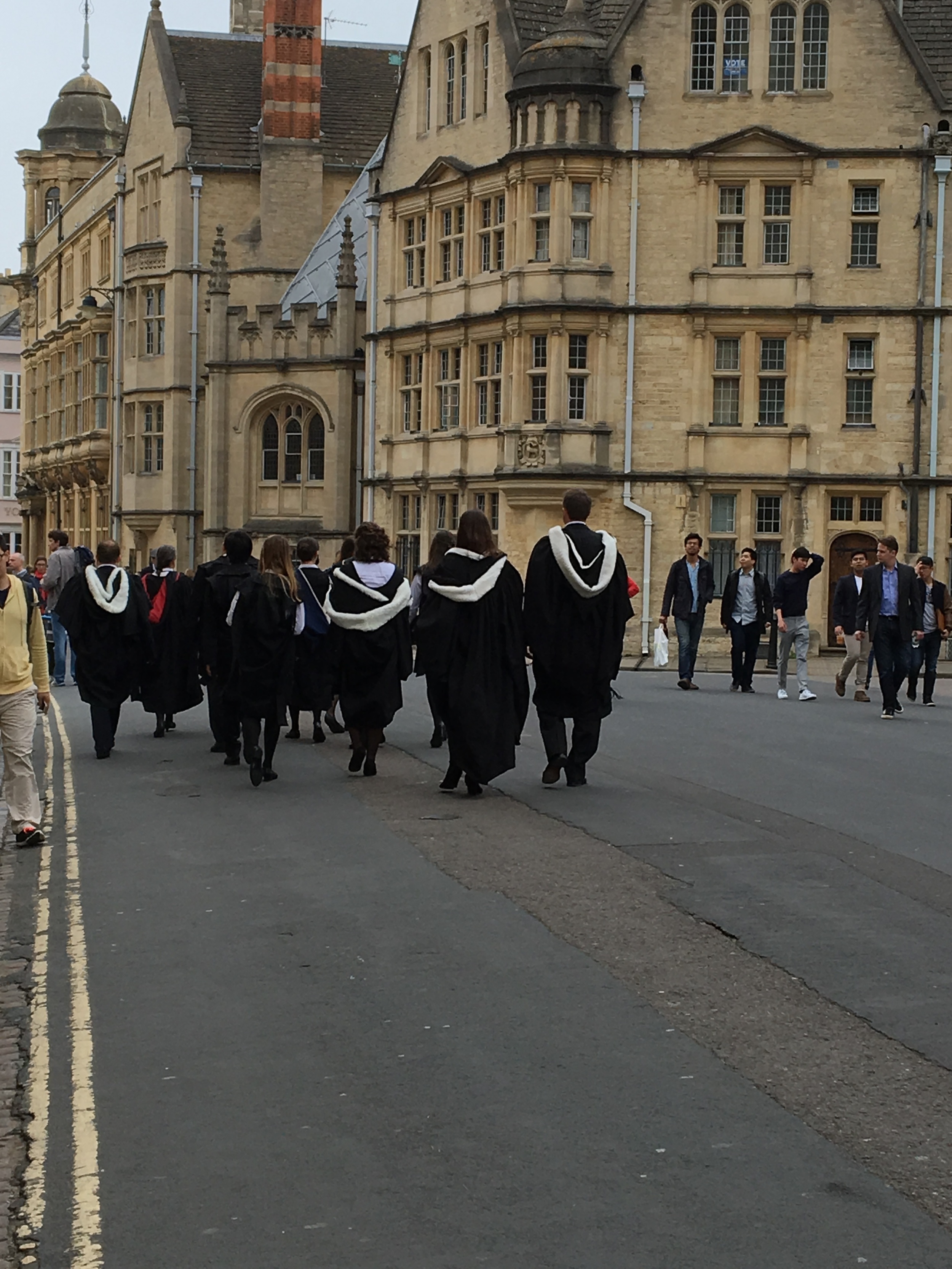 A group of students led by their faculty member make their way in full regalia on foot to their graduation ceremony. 