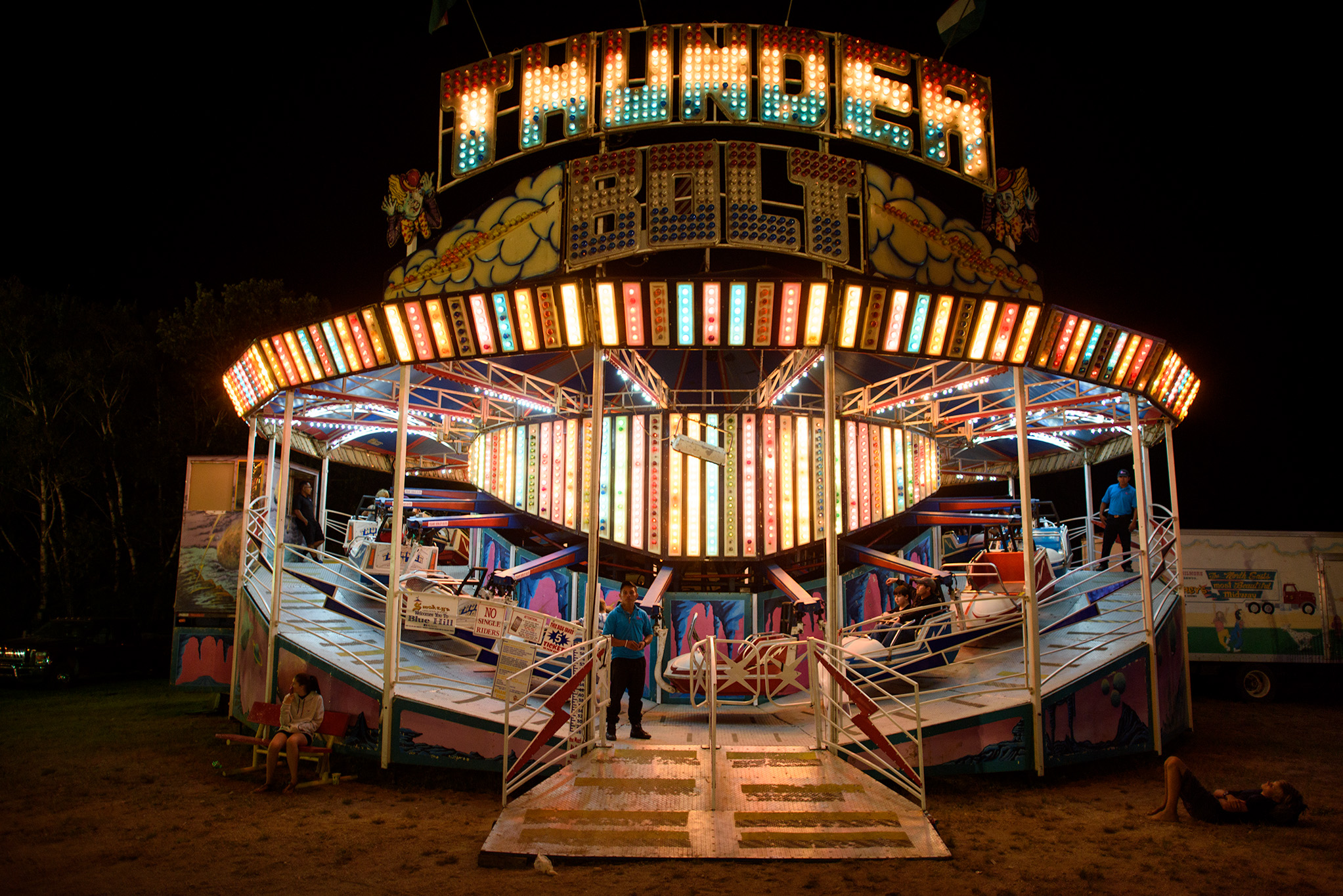 Attendants wait for more takers before running the Thunder Bolt, while a young boy, who lives in a town without a store, or street lights, lies on the ground to watch the dazzling light display. 