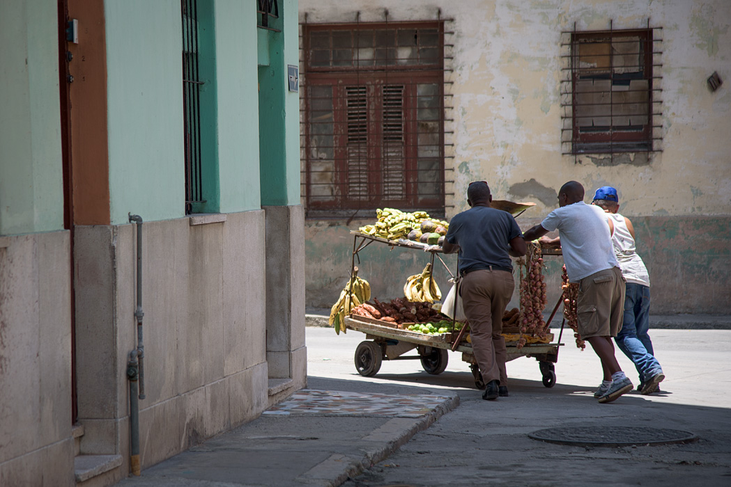 Three men struggle to maneuver a fruit cart in the streets.