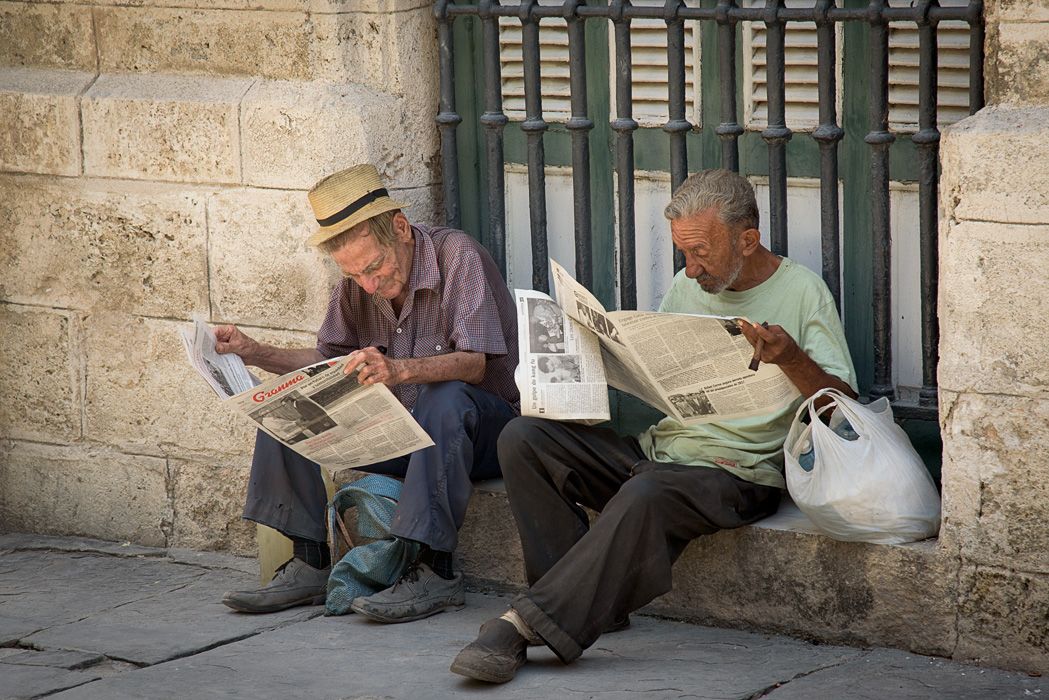 Two gentlemen read the news on the stoop on the outskirts of Old Havana