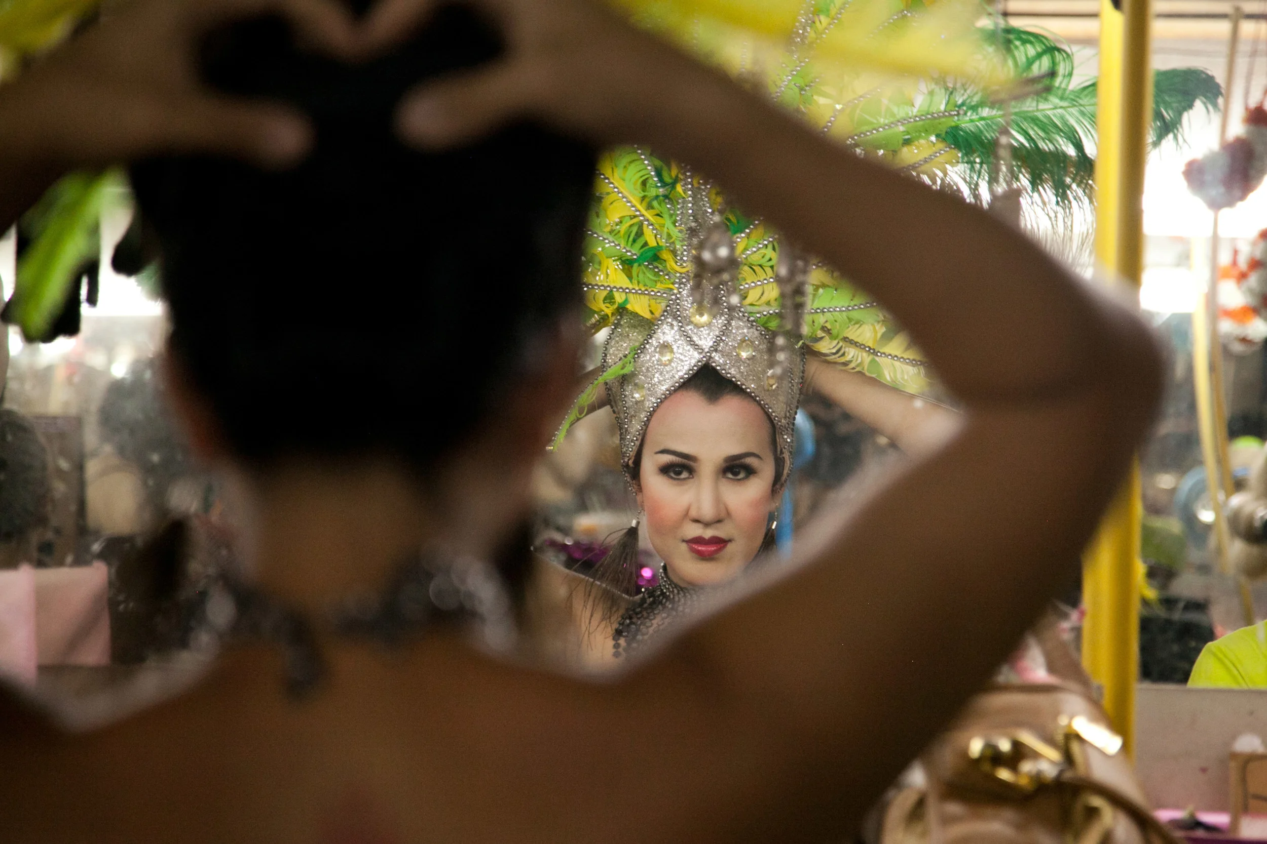 A dancer settles a large and elaborate headdress on her head before heading out to the night market to attract tourists to the Chiang Mai Cabaret Show. The show is held at a small bar in the city's market district, and is the only cabaret show in Chiang Mai. (27 April 2013, Chiang Mai, Thailand)