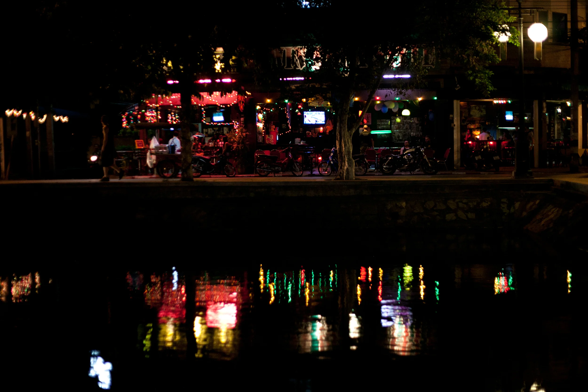 A bar's colorful lights gleam in the moat in Chiang Mai's red light district. The city attracts millions of tourists, from backpackers to high-powered businessmen, who come for the festivals, the temples, the nature, and the bar girls. (April 2013)