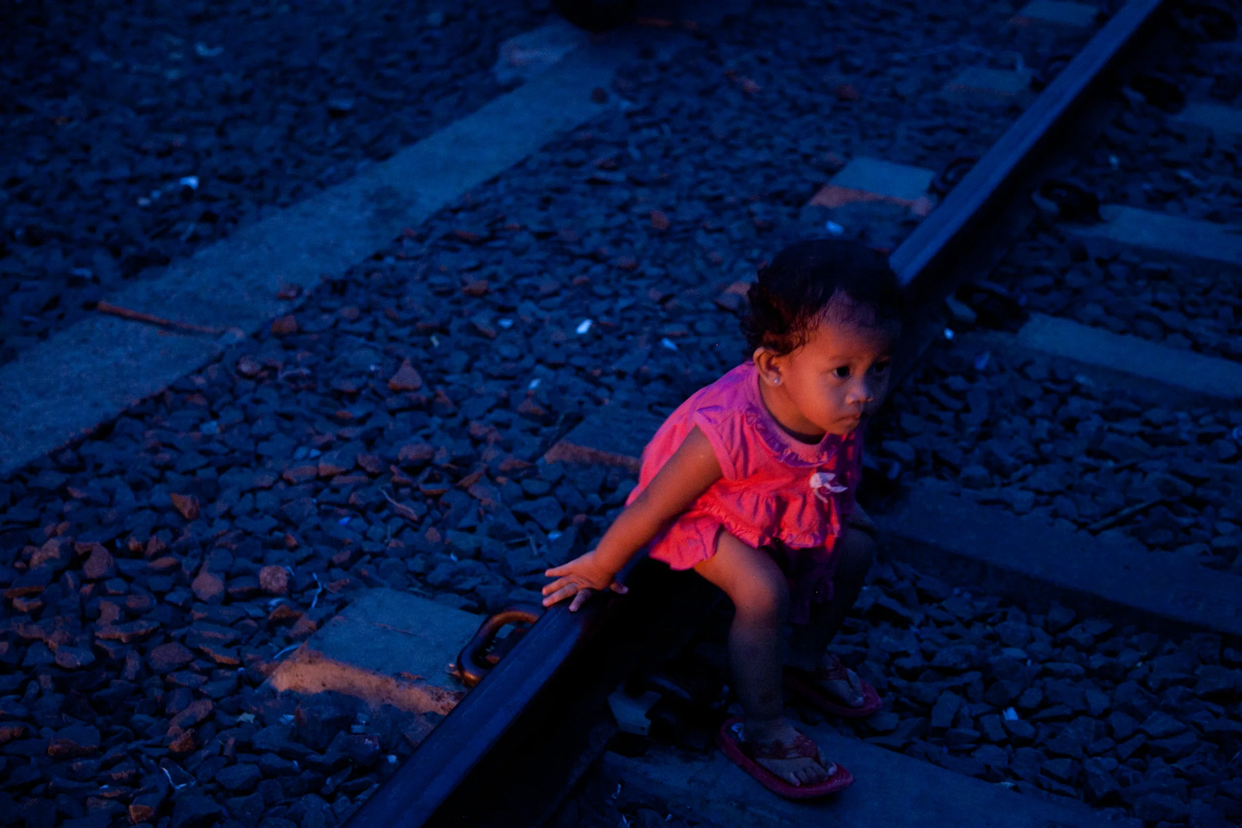 The firelight of burning trash casts a warm glow on a little girl sitting on the train tracks that run through one of Jakarta's slums. (27 May 2013)