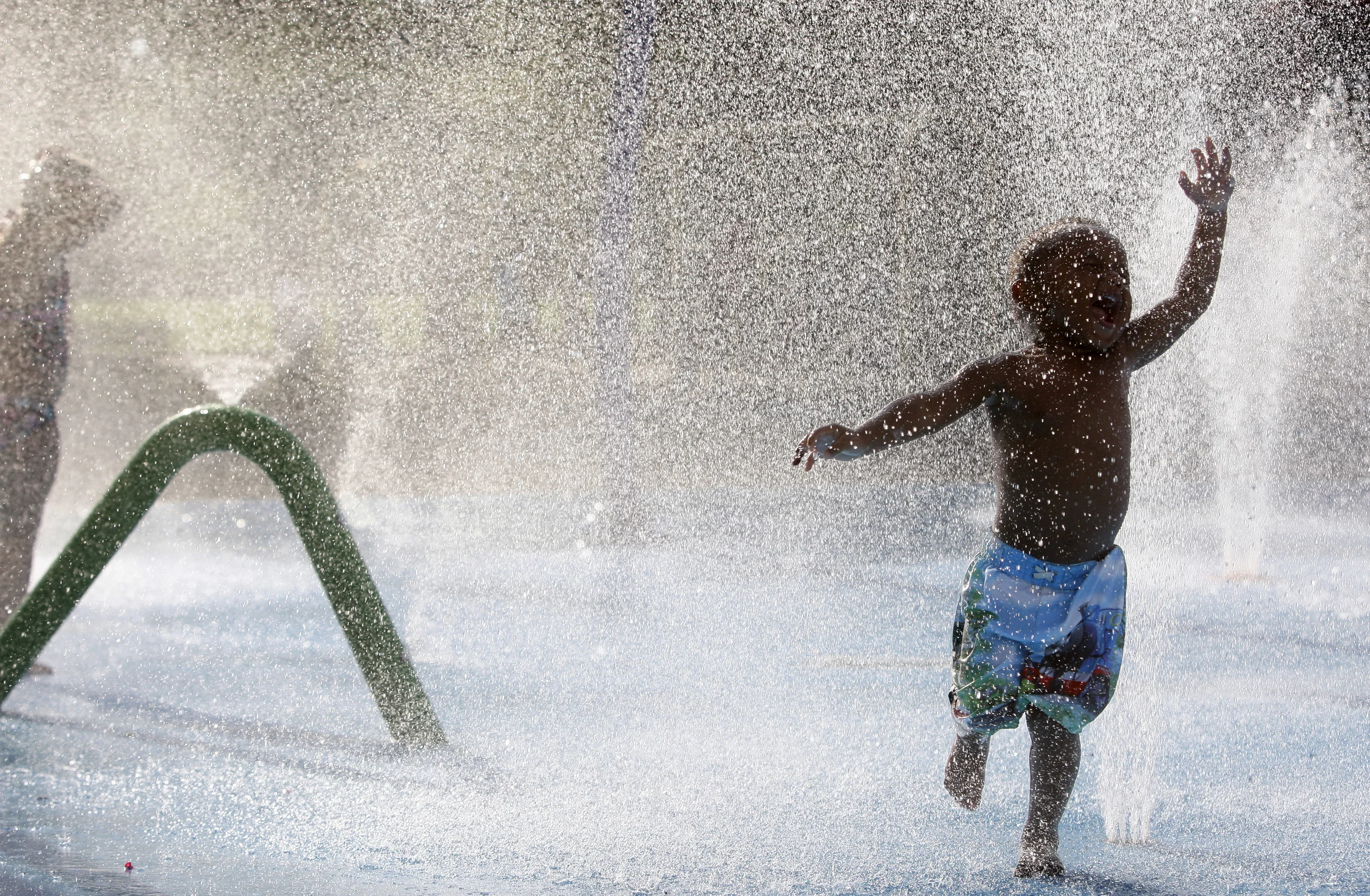  Two-year-old Jaidan Slater plunges through a water fountain to cool off in the 91 degree heat at Play-for-All-Park in South Jacksonville. 
