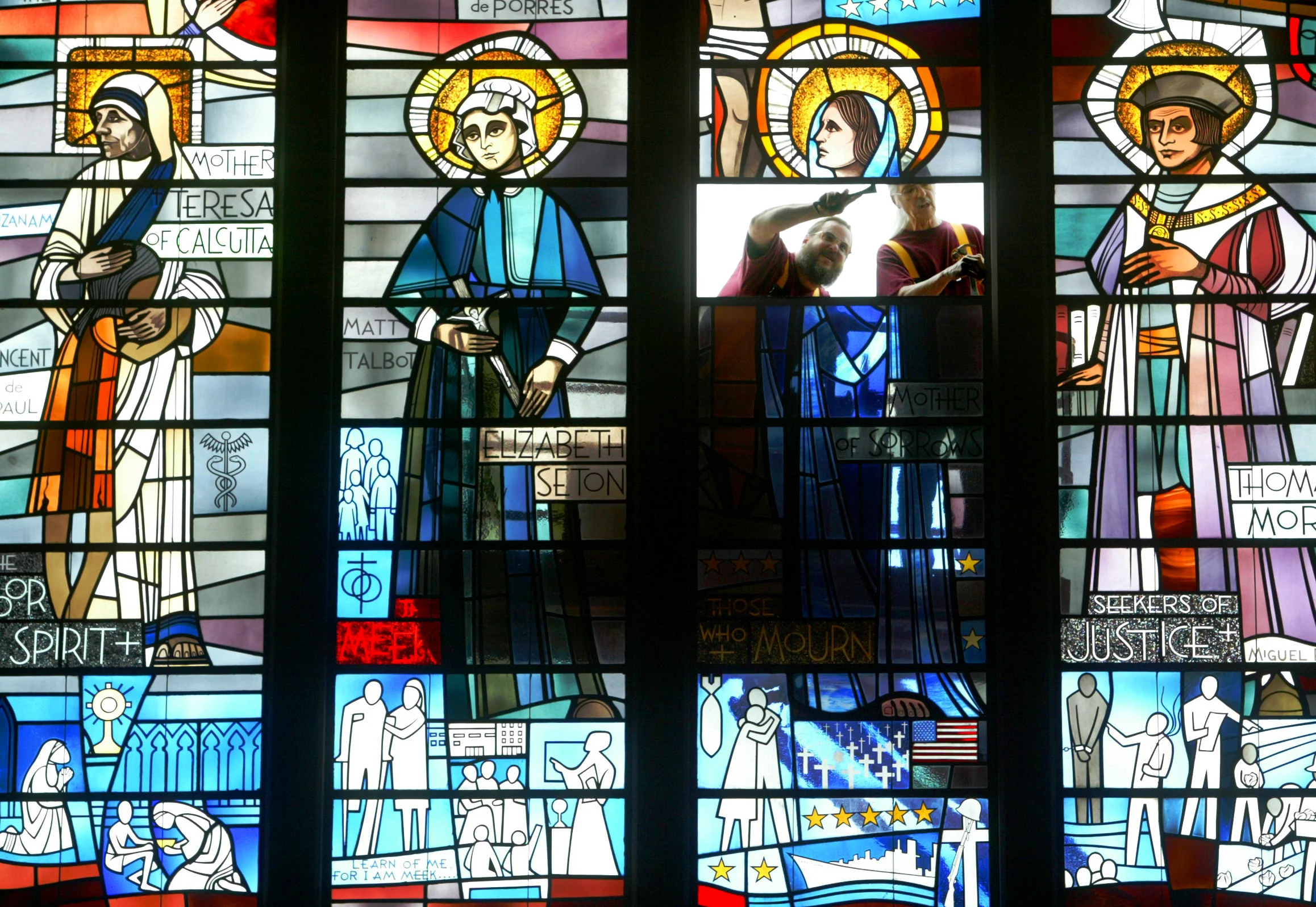  Doug Potter (left) and Merle Steward, of Jacksonville Art Glass, install a repaired panel of the “Mother of Sorrows” stained glass window at Our Saviour Church in Jacksonville.&nbsp; 